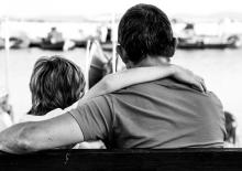 Nastolatek siedzący na ławce w parku, zamyślony, z książką na kolanach, otoczony przyrodą.