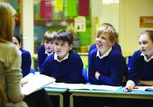 Dziecko z plecakiem stojące przed budynkiem nowej szkoły, z uśmiechem na twarzy