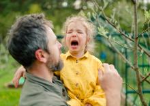 Złoszczące się dziecko obok spokojnego rodzica, który pomaga mu się uspokoić