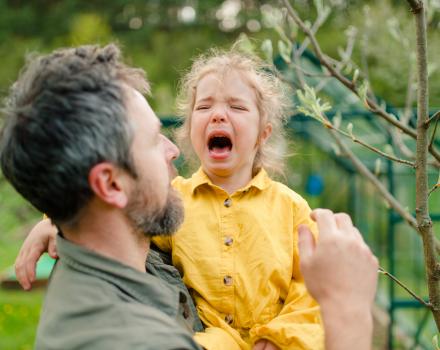 Złoszczące się dziecko obok spokojnego rodzica, który pomaga mu się uspokoić